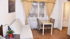 A cozy living room with a sofa, a small table with a lamp, a dining table with chairs, and a window with curtains. - West Apartments Hoża 36 (Warsaw)