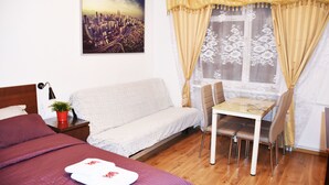 A hotel room with a bed, a sofa, a dining table with chairs, a small table with a plant, and a window with curtains. - West Apartments Hoża 36 (Warsaw)