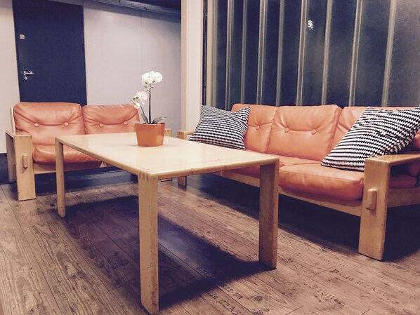Ein Zimmer mit Holzboden, einer Couch mit gemusterten Kissen, einem kleinen Tisch und einem Blumentopf.