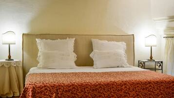 A bed with a beige headboard, two white pillows, and a red patterned bedspread. There are two bedside tables with lamps.