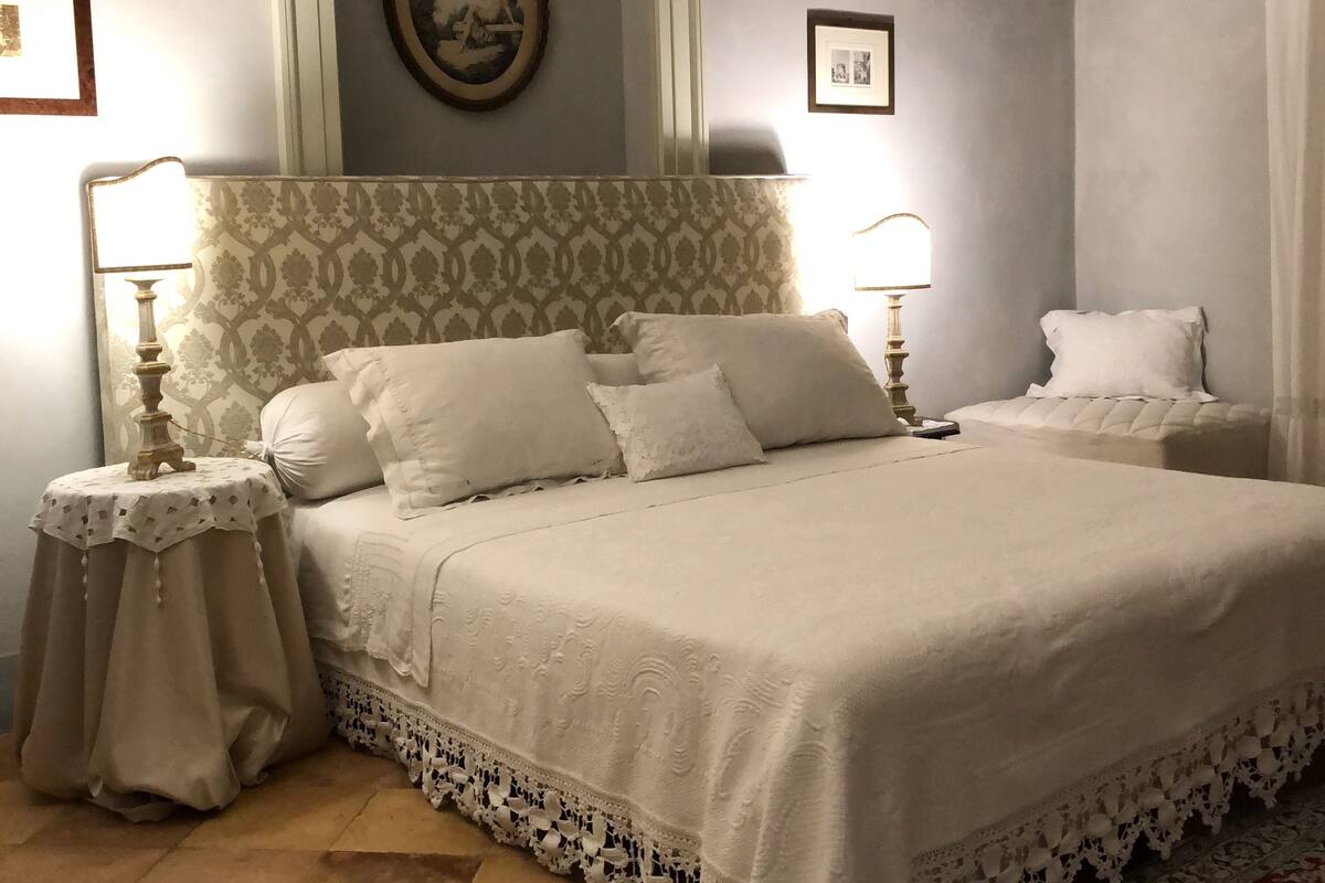 Un dormitorio ordenado con una cama grande, dos mesitas de noche con lámparas, un cabecero estampado y un espejo decorativo.
