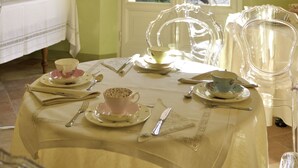 Uma sala de jantar com mesa posta para quatro pessoas, janela com vista para um jardim e um candelabro na parede.