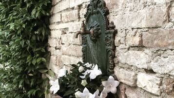 Eine Steinsäule mit einem verzierten Metall-Wasserhahn und einem Pflanzgefäß mit weißen Blüten.