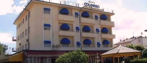 Et hotel med flere etager, der har et skilt med teksten "Colombo". Der er en central gårdsplads med en springvand og en pavillon.