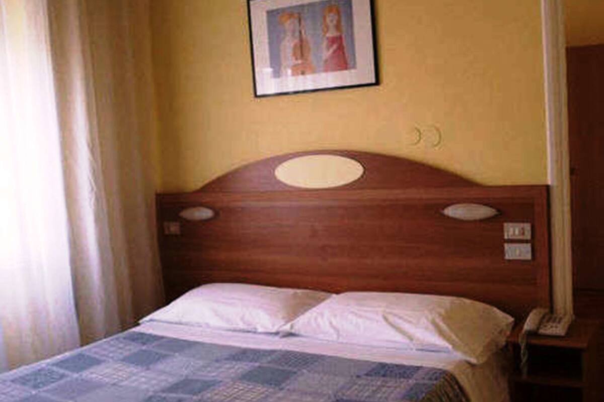 Ein Einzelbett mit hölzernem Kopfteil, ein Nachttisch mit Lampe sowie ein gerahmtes Bild an der Wand.