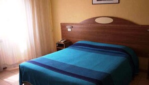 Un lit simple avec une couvre-lit à rayures bleues et violettes, dans une chambre dotée d’une tête de lit en bois et d’une petite table de chevet avec une lampe.