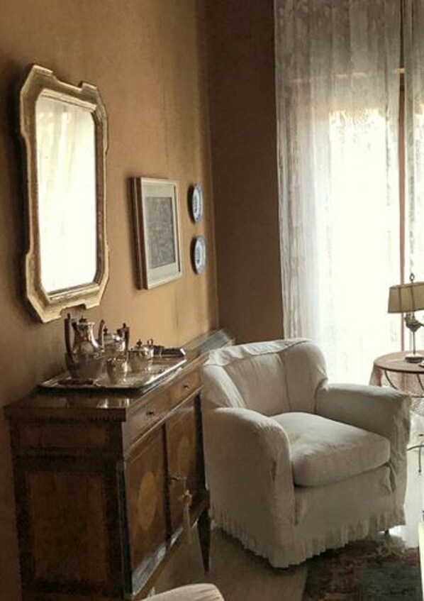A room with a beige armchair, a wooden cabinet, a mirror, and a small table with a lamp.