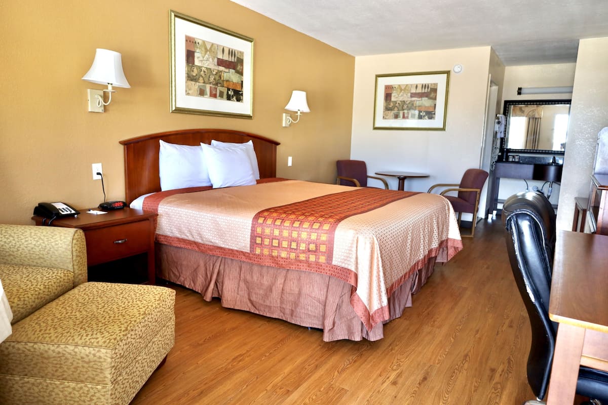 A hotel room with a large bed, two bedside tables, a desk, a chair, and a small table with a lamp.