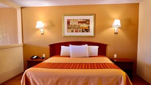 A hotel room with a large bed, two bedside tables, a telephone, and two wall-mounted lamps. - Regency Inn & Suites (Gladewater)