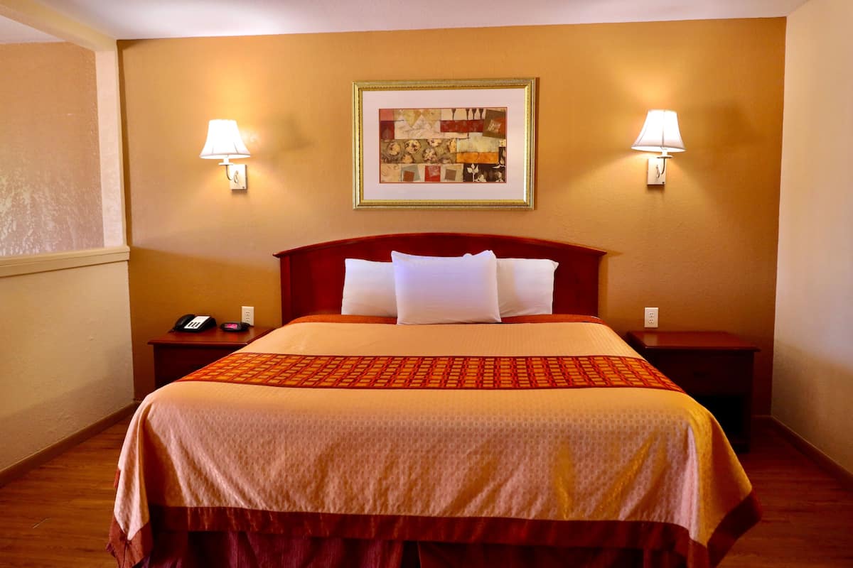A hotel room with a large bed, two bedside tables, a telephone, and two wall-mounted lamps.