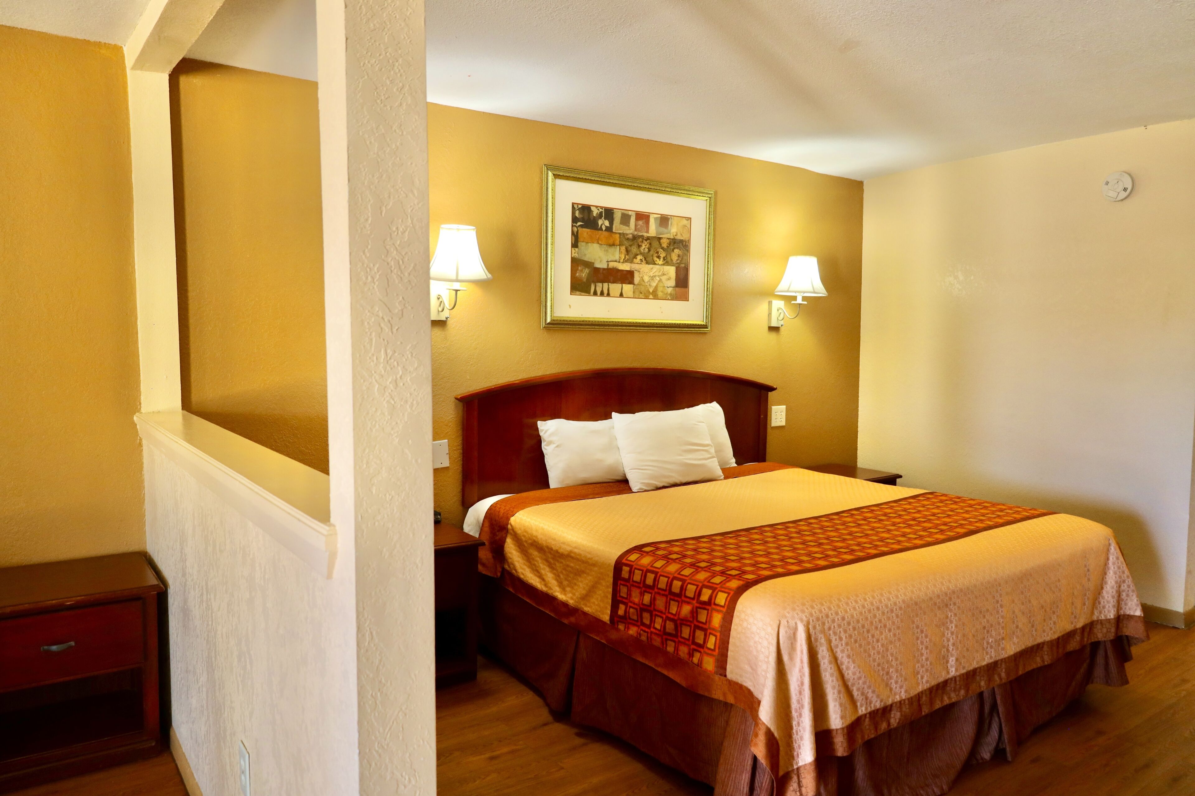 Habitación de hotel con cama, dos lámparas de noche, un cuadro en la pared y una mesita de noche de madera.