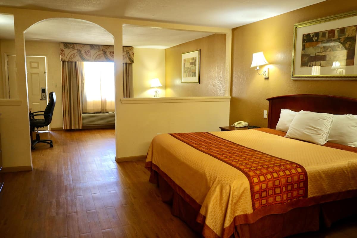 A hotel room with a large bed, a desk, and a chair. There is a door leading to another room and a window with curtains.