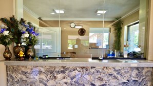 A marble reception desk with decorative vases, a clock, and a view of the outside. - Regency Inn & Suites (Gladewater)