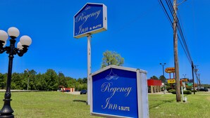 A blue sign for Regency Inn & Suite with a white border, located in a grassy area with a clear blue sky. - Regency Inn & Suites (Gladewater)