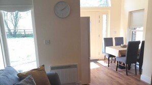 A living room with a sofa, a patterned rug, a clock, and a dining area with chairs and a table. - Delphi Lodge (Ashbourne)