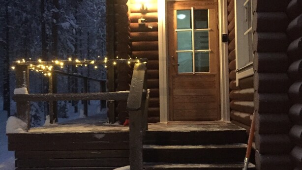 Una cabaña de troncos con puerta de madera, un porche con escalones y un techo cubierto de nieve.