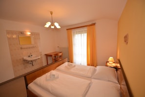 Een hotelkamer met een bed, nachtkastje met lamp, een klein tafeltje met stoel, spiegel en raam met gordijnen.