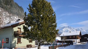 Un edificio con balcón, una banca y una montaña nevada al fondo.