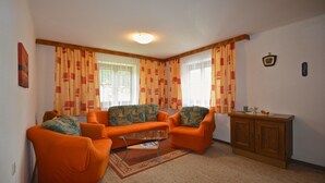 Una sala de estar con dos sillones naranjas, un sofá estampado, una mesa de centro y un aparador de madera.