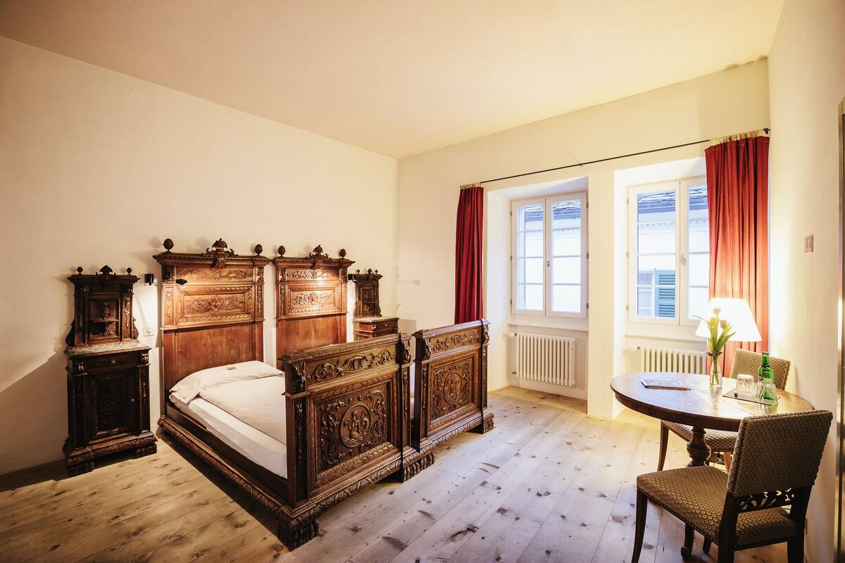 A bedroom with a wooden bed, a nightstand, a dresser, and a window with curtains.