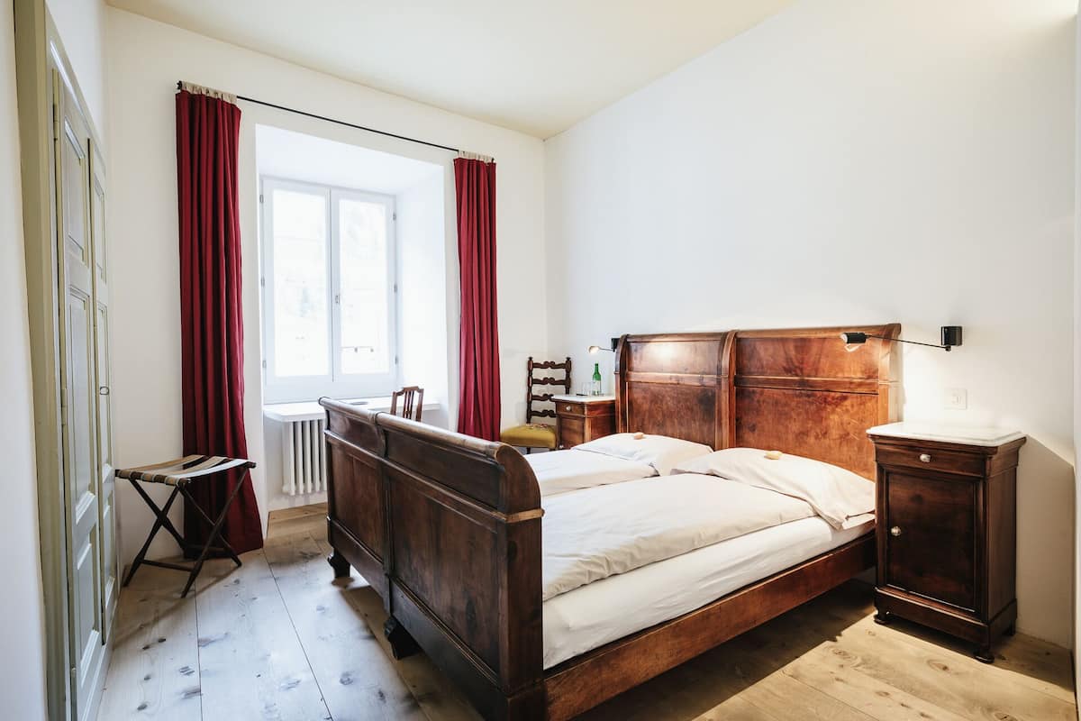 A bedroom with a wooden bed, a bedside table, a chair, and a radiator.