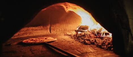 A pizza oven with a pizza inside, a wooden table, and a brick floor.