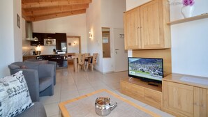 Un espacio habitable amplio con un sofá, televisión, armarios de madera y una cocina al fondo.