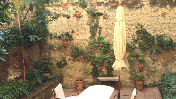 An outdoor patio with a table and two chairs, surrounded by potted plants and a stone wall. - Casa al Teatro (Verona)