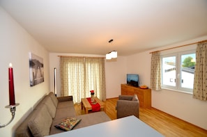 A living room with a sofa, a small table, a TV, and a window with curtains.