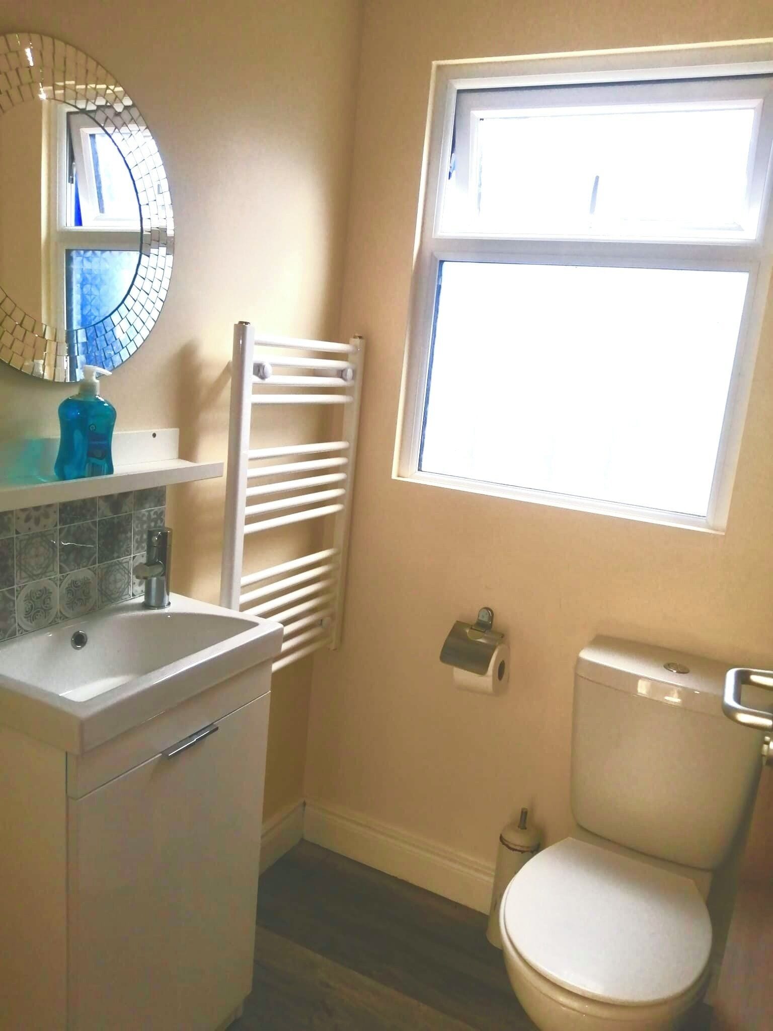 A bathroom with a white sink, a mirror with a mosaic design, a toilet, and a window with blinds.