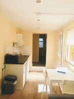 Una cocina compacta con encimera negra, armarios blancos, un pequeño cubo de basura y una ventana con persianas.