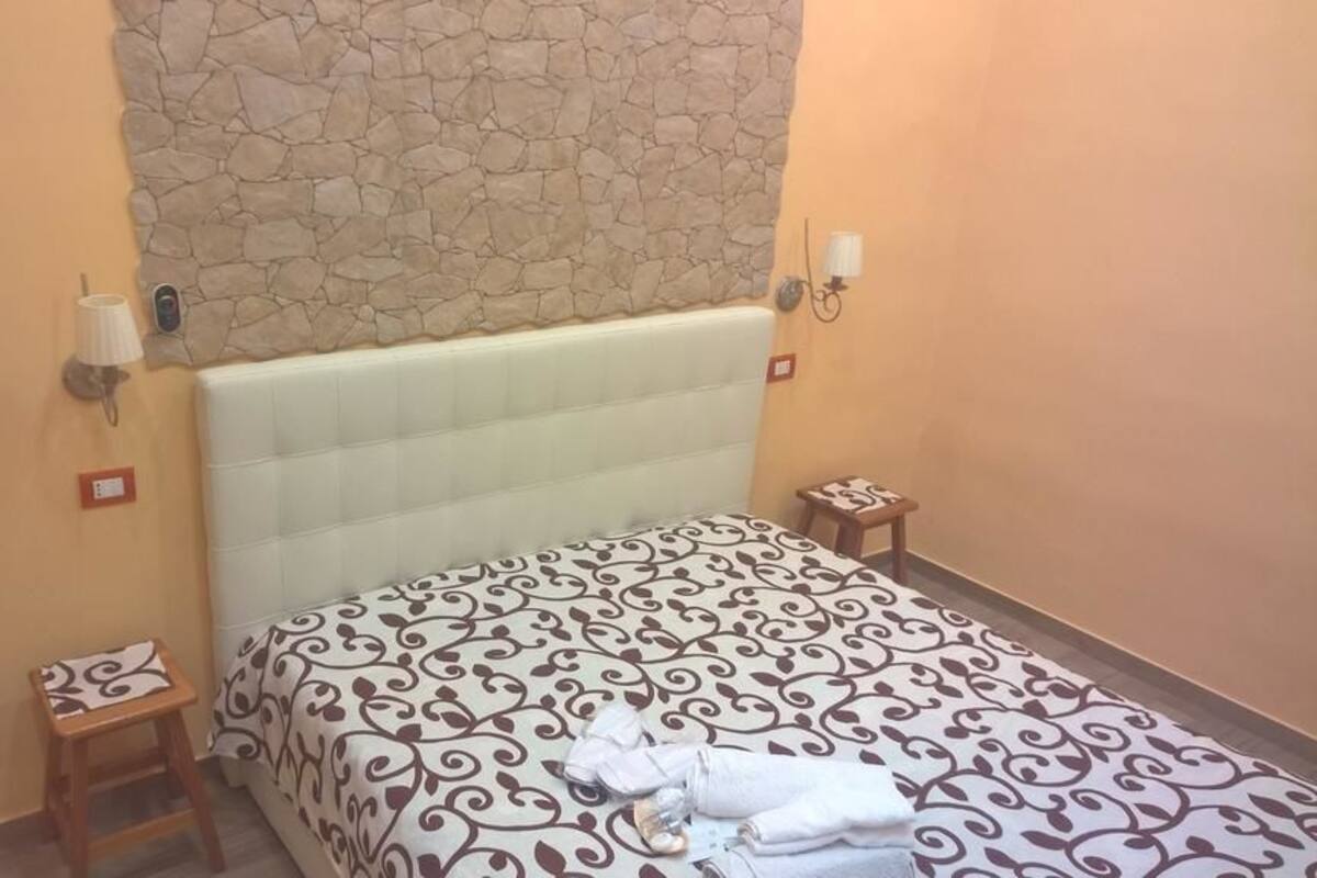 Una habitación de hotel con una cama, un taburete de madera y una mesita de noche con lámpara.