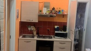 A compact kitchen with a gas stove, oven, and sink. There is a small dining area with a table and chairs. The kitchen has orange walls and a tiled backsplash. - B&B Anny (Naples)