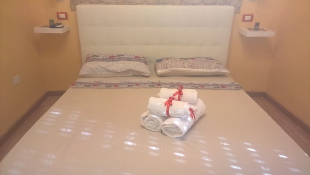 A hotel room with a neatly made bed, two pillows, and two bedside tables with small decorative items. - B&B Anny (Naples)