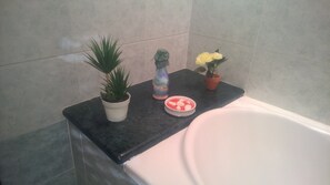 Une salle de bain avec une baignoire, un comptoir agrémenté d’une plante en pot, un objet décoratif et un bol de sels de bain.