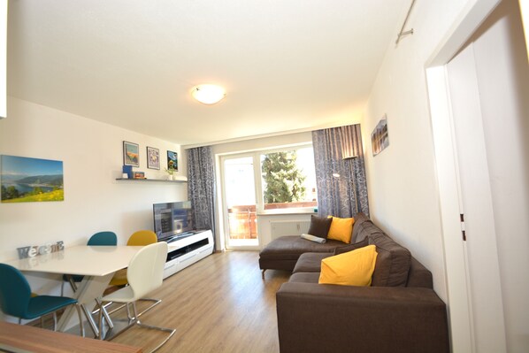 A modern living room with a dining area, a sofa with yellow cushions, and a television.
