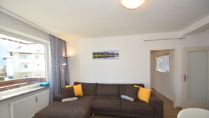 Ein Wohnzimmer mit einem braunen Ecksofa, einem kleinen Tisch und einem Fenster mit Blick auf Gebäude.