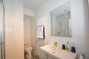 A bathroom with a toilet, a sink with a mirror, and a shower area.