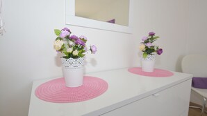 Zwei weiße Schränke mit rosa Platzsets und weißen Vasen mit lila und weißen Blumen.