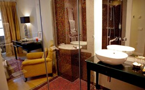 Een moderne badkamer met een douchecabine van glas, twee wastafels en een gele fauteuil.