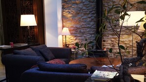 Una sala de estar acogedora con un sofá, una mesa de centro y una lámpara. En el fondo, una pared de piedra y una puerta de madera.