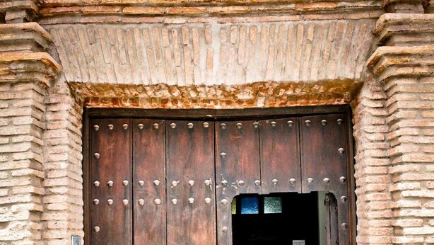 Una puerta de madera grande con remaches metálicos, en un edificio de ladrillo.