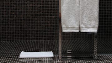 Une salle de bain avec un mur carrelé, une serviette blanche suspendue à un porte-serviettes et une autre serviette blanche posée sur le sol.