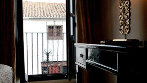 Habitación de hotel con una cama, un escritorio, una lámpara y vistas a un edificio por una puerta abierta.