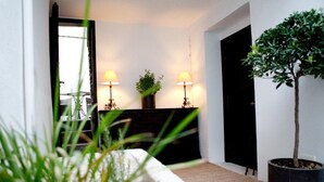 Una sala moderna con un sofá, dos lámparas de pie, una planta en maceta y una puerta.