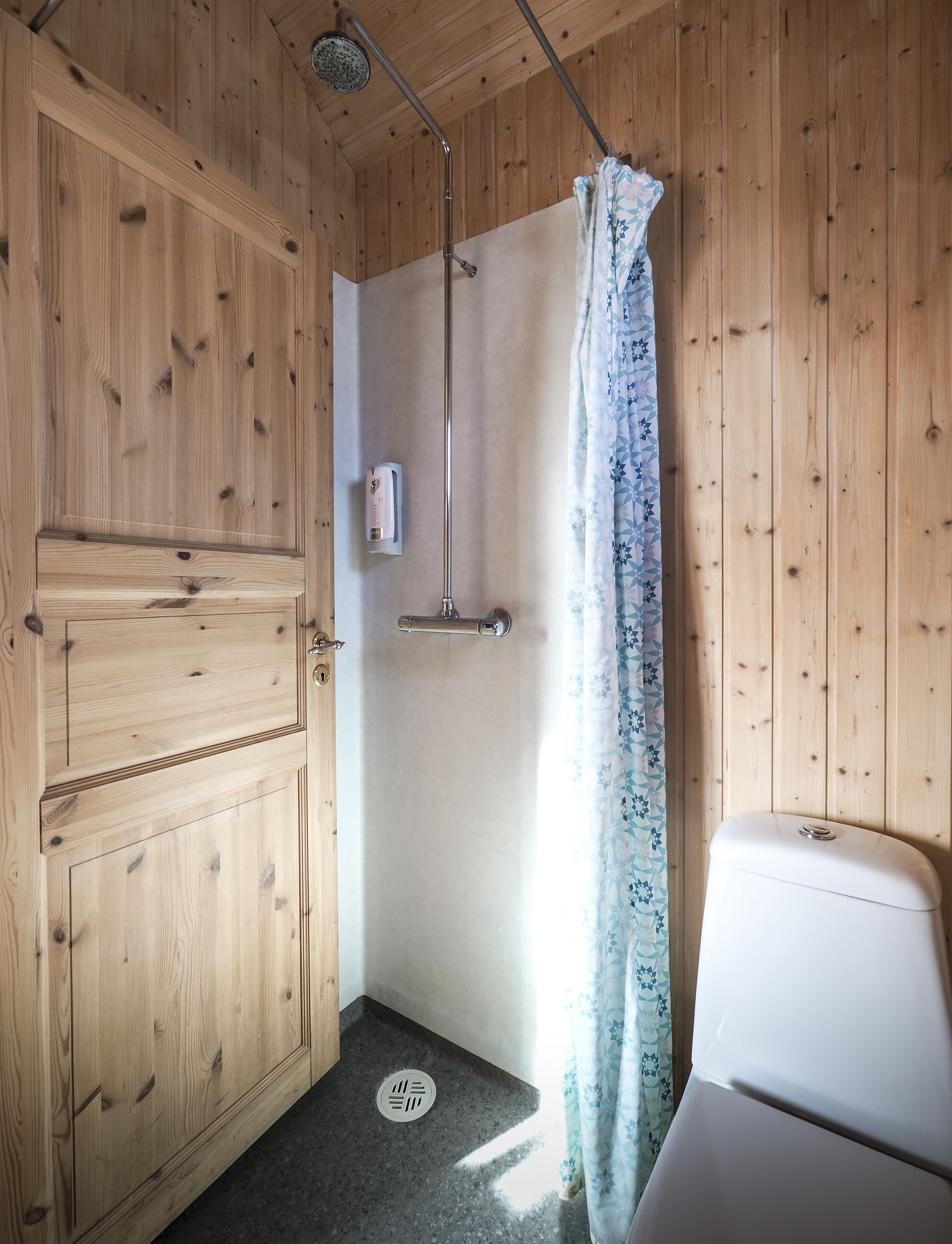 A wooden cabin bathroom with a shower, toilet, and a hand soap dispenser.