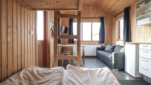 Un intérieur de chalet chaleureux avec un lit, un canapé, un téléviseur et une petite cuisine.