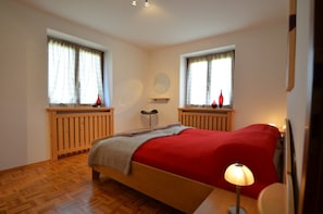 A bedroom with a bed, two windows with curtains, a bedside table, a lamp, and a mirror on the wall. - Foxes Mountain View by Z-K-H Rentals (Leogang)