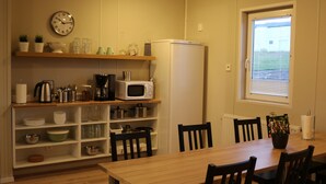 Une cuisine compacte avec une table en bois, des chaises noires, un four à micro-ondes, un réfrigérateur et une horloge au mur.
