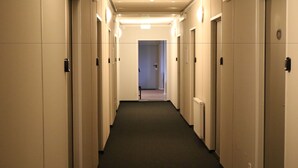 Un couloir d’hôtel avec des portes des deux côtés, un sol recouvert de moquette et un luminaire au plafond.